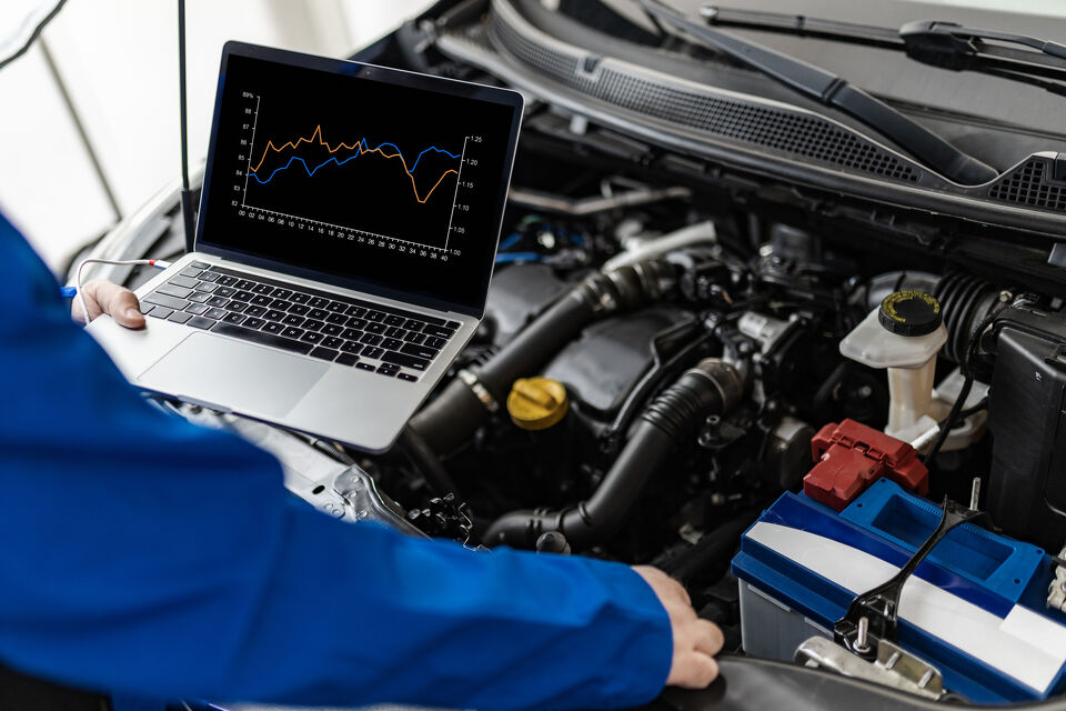 Mechanic reviewing diagnostic data on a laptop beside an open engine bay