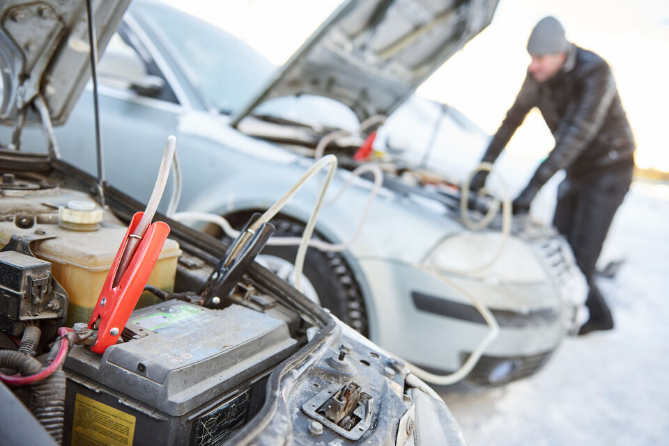 Jumper cables connected to a car battery for a roadside jump start in snow