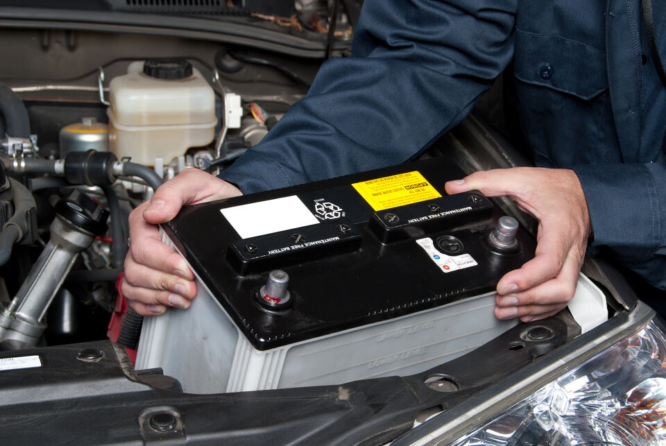 Mechanic's hands fitting a battery into a car's engine bay