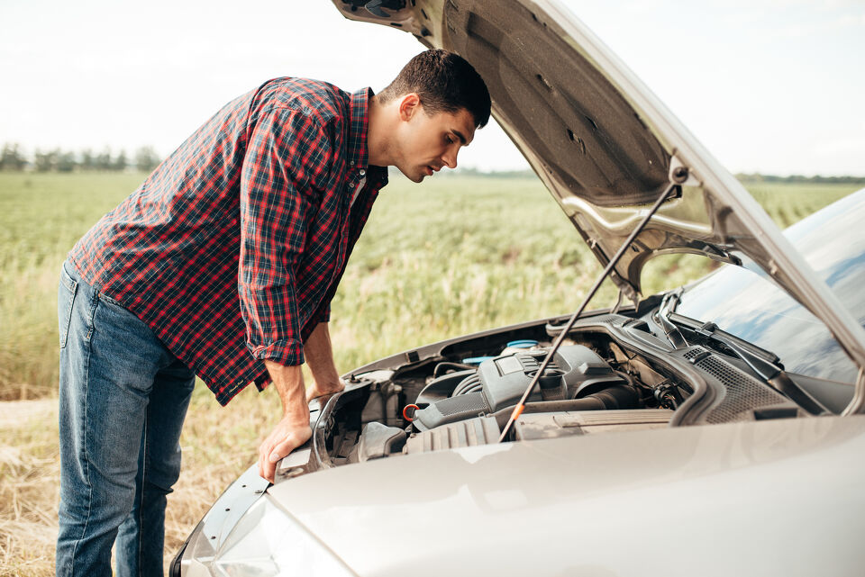 Man leaning over his car's open bonnet in a rural field after a breakdown