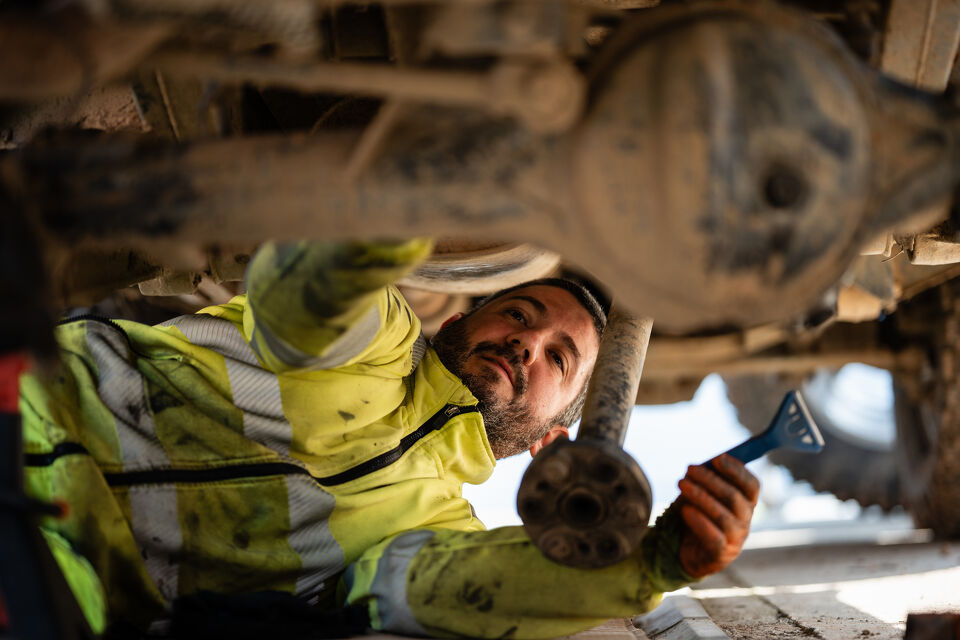 Mechanic in hi-vis lying underneath a vehicle inspecting the axle and hub