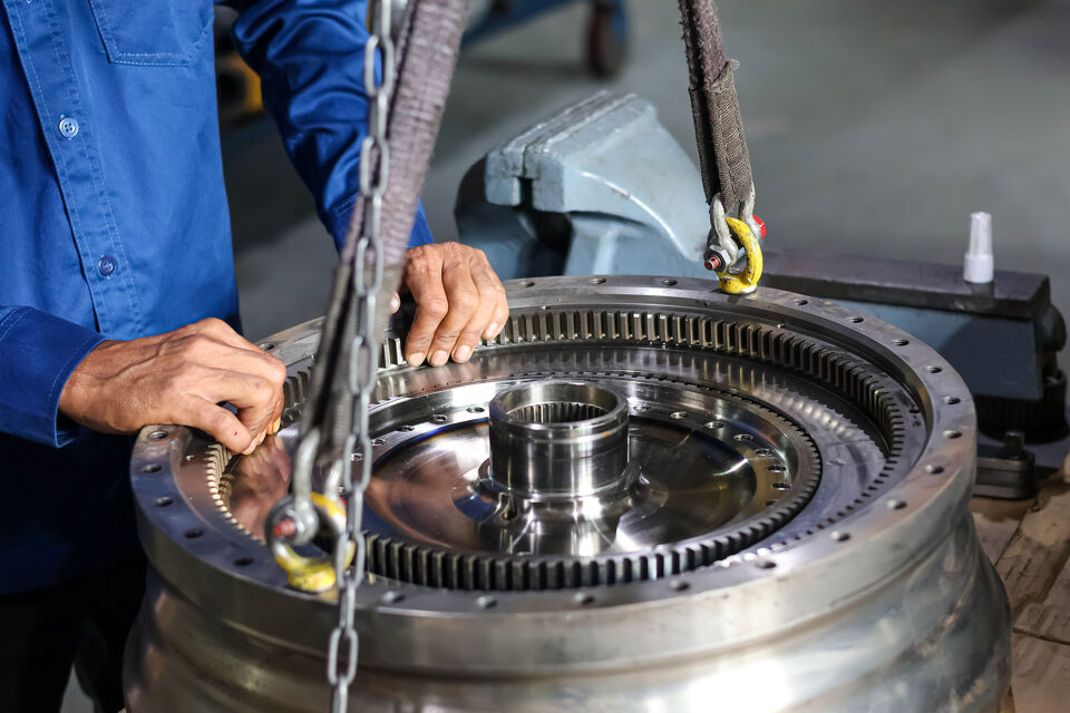 Mechanic using a chain hoist to lift a large transmission ring gear
