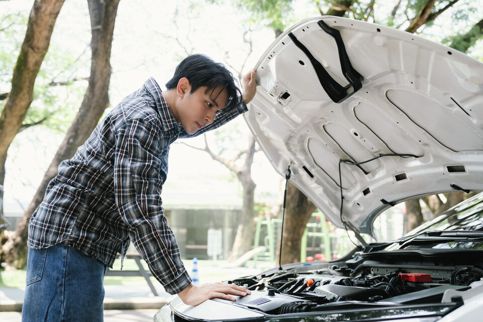 Man inspecting his car's engine bay after breaking down at the roadside