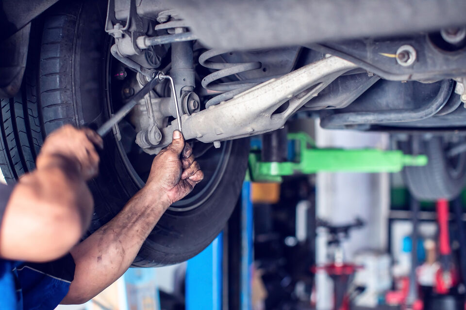 Mechanic's hands adjusting a rear shock absorber underneath a car