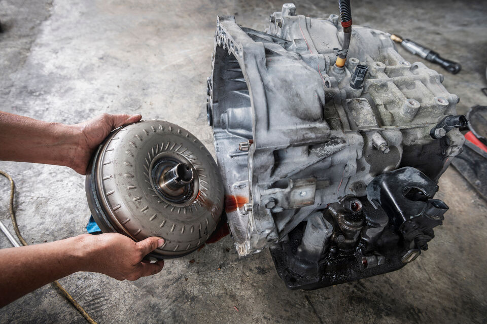 Hands holding a torque converter beside a removed transmission casing