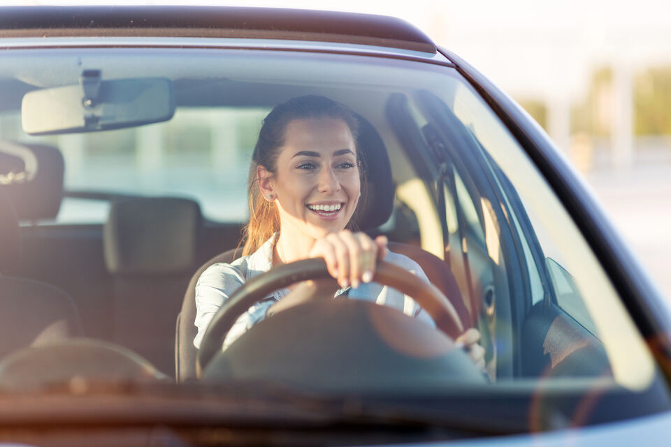 Smiling woman driving a car, viewed through the windscreen