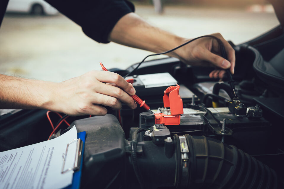 Mechanic testing an electrical component in an engine bay with a multimeter