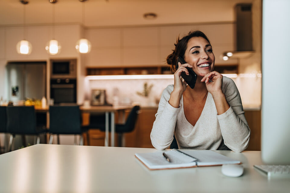 Woman smiling on a phone call while working at a kitchen bench
