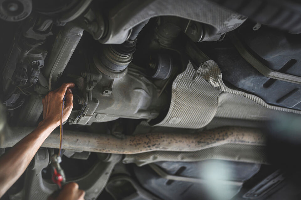Mechanic's hand reaching up into a vehicle's underside near the driveshaft