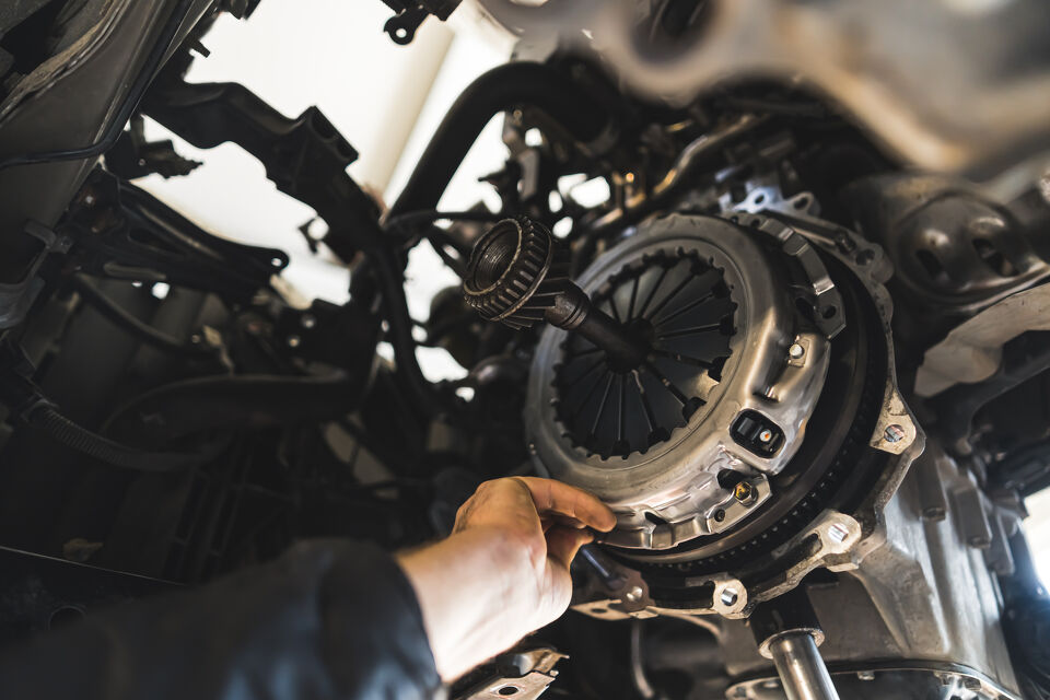 Mechanic's gloved hand fitting a clutch plate onto a vehicle's flywheel