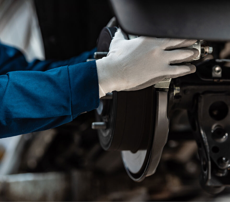 Gloved hand inspecting a rear brake drum and wheel hub under a car
