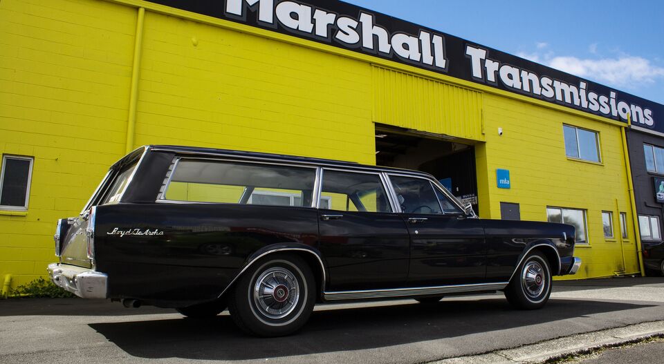 Classic black station wagon parked outside the yellow Marshall Transmissions building