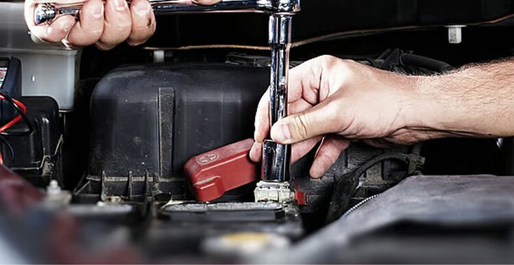 Mechanic using a ratchet on a car battery terminal in an engine bay